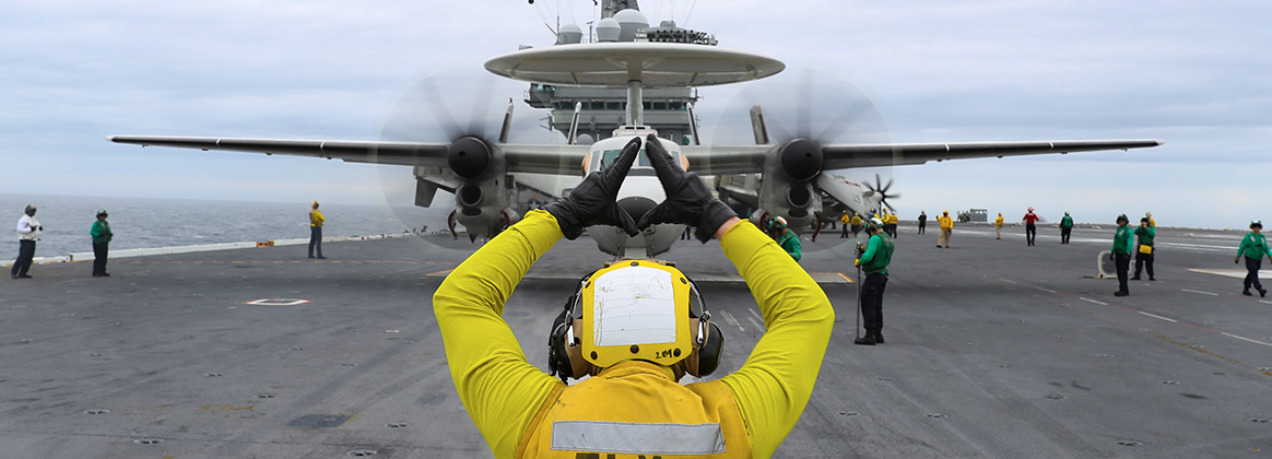 Aviation Boatswain's Mate (Handling) 3rd Class Trevor Prosser directs an E-2D Hawkeye